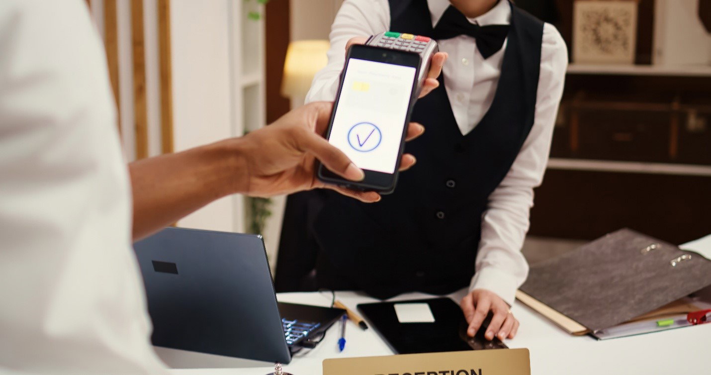 TechDogs-"An Image Showing Hotel Receptionist Accepting A Mobile Payment From A Guest"