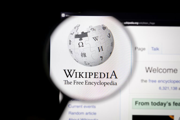 TechDogs-"Wikipedia Urges AI Firms To Use Its Paid API And Stop Scraping"-"Close-Up Of Wikipedia Logo Viewed Through A Magnifying Glass On A Computer Screen"
