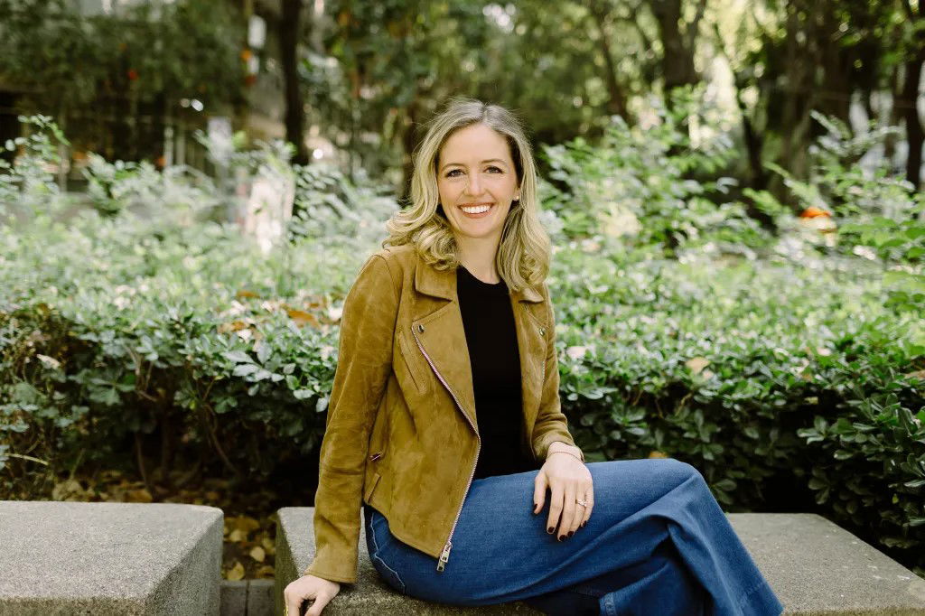 TechDogs-"Leona Health Raises $14M To Fix WhatsApp Overload for Doctors"-"Leona Health Founder Caroline Merin Seated Outdoors, Smiling During An Interview In A Park Setting"