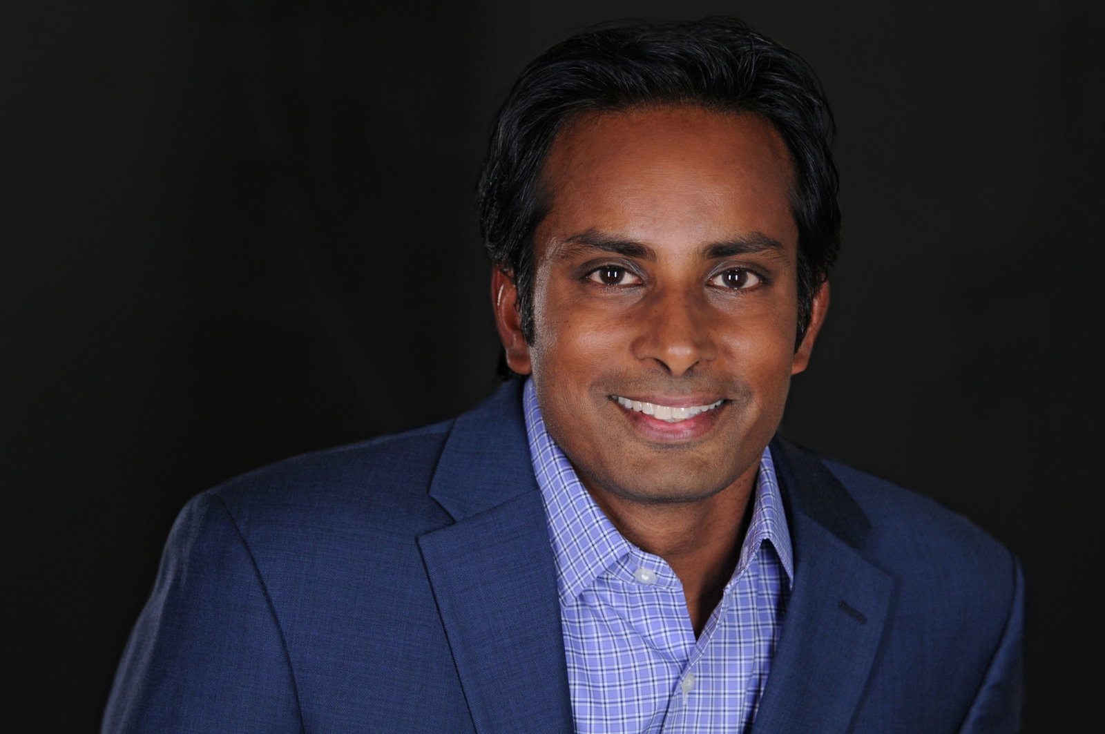 TechDogs-"What Is The Impact Of Network Outages?"-"Professional Headshot Of New Relic CEO Ashan Willy Smiling In A Blue Suit Against A Dark Background"